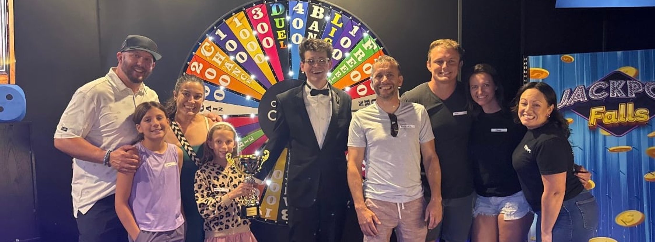 Family group with their game show host in front of the prize wheel at ClueClock Gameshow