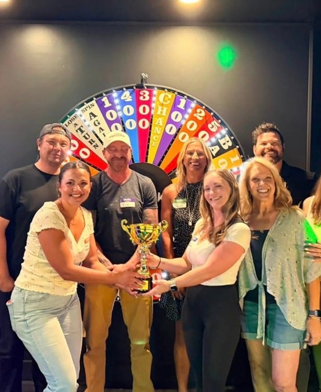 Winning team hoisting the trophy in front of the prize wheel at ClueClock Gameshow